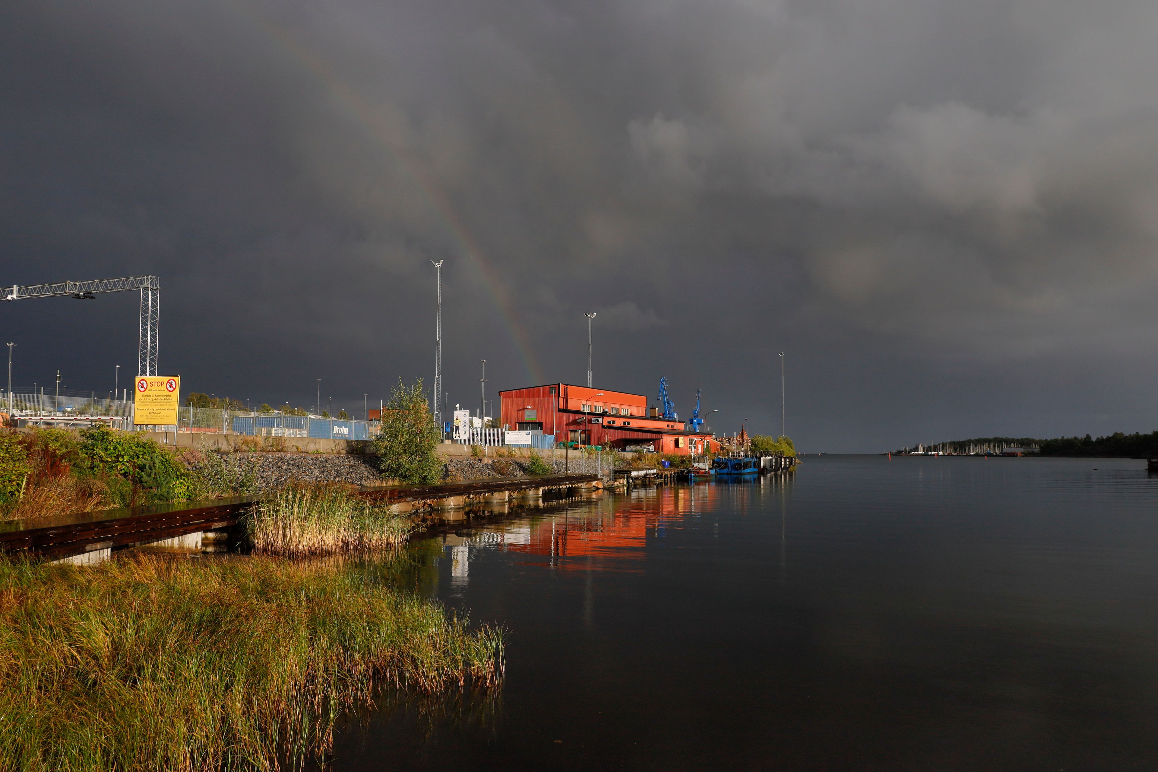 Ein Hafen mit einem roten Gebäude, einem Kran und einem Regenbogen.