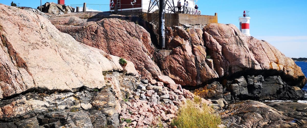 A red lighthouse and a red building on rocky terrain.