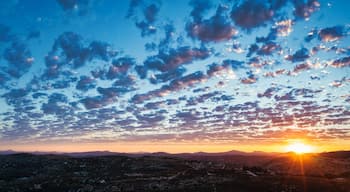A sunset over a mountainous landscape with scattered clouds.
