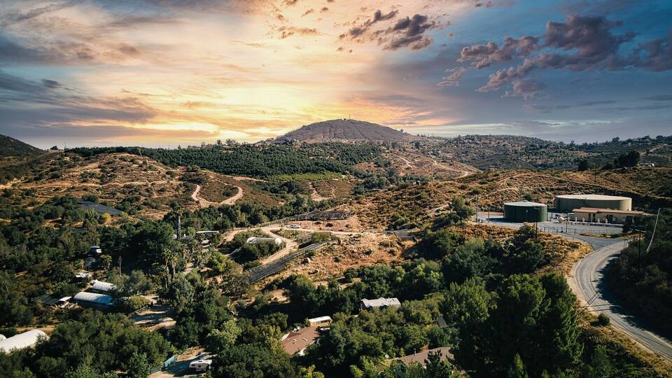 A mountainous landscape with a winding road, a large building, and dense forested areas.