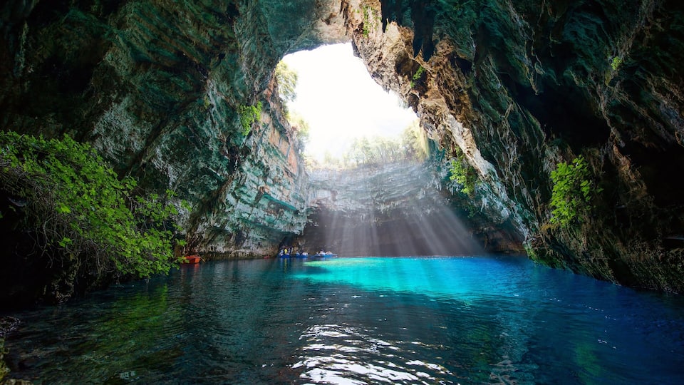 A cave with a natural archway, clear turquoise water, and lush greenery.