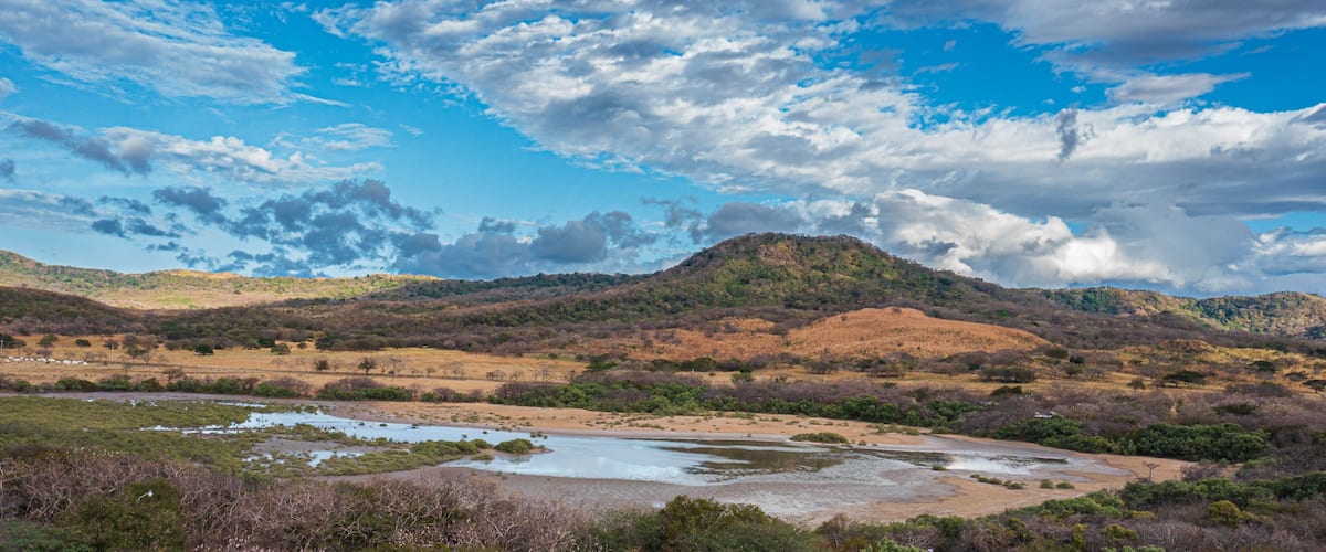 A river winding through a hilly landscape with a mountain in the background and a partly cloudy sky.
