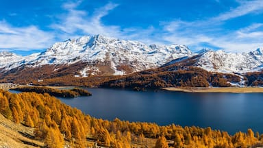 A mountainous landscape with a lake surrounded by autumn-colored trees and snow-capped peaks.