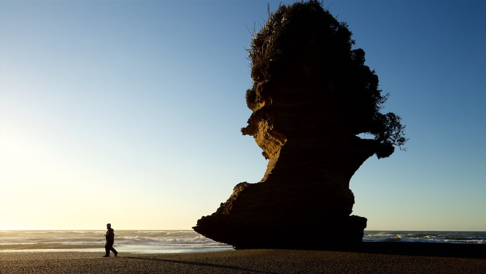A person walking on a beach with a large rock formation in the background.