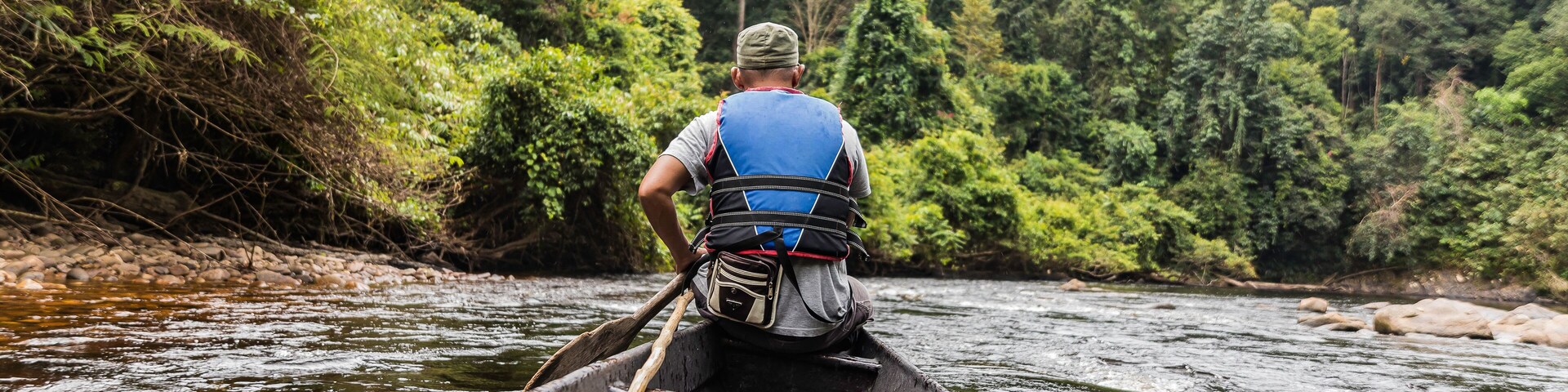 Una persona remando un canoa por un río rodeado de bosque denso.