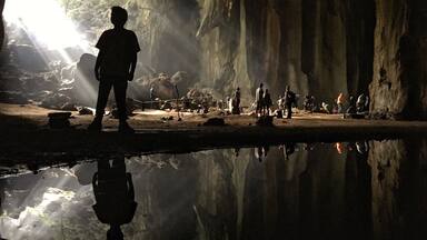 A cave with a reflective water surface and people gathered inside.