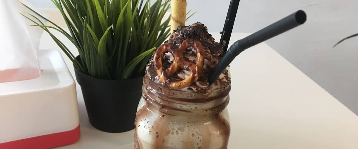 A jar of iced coffee with a straw and a spoon, placed on a white plate.