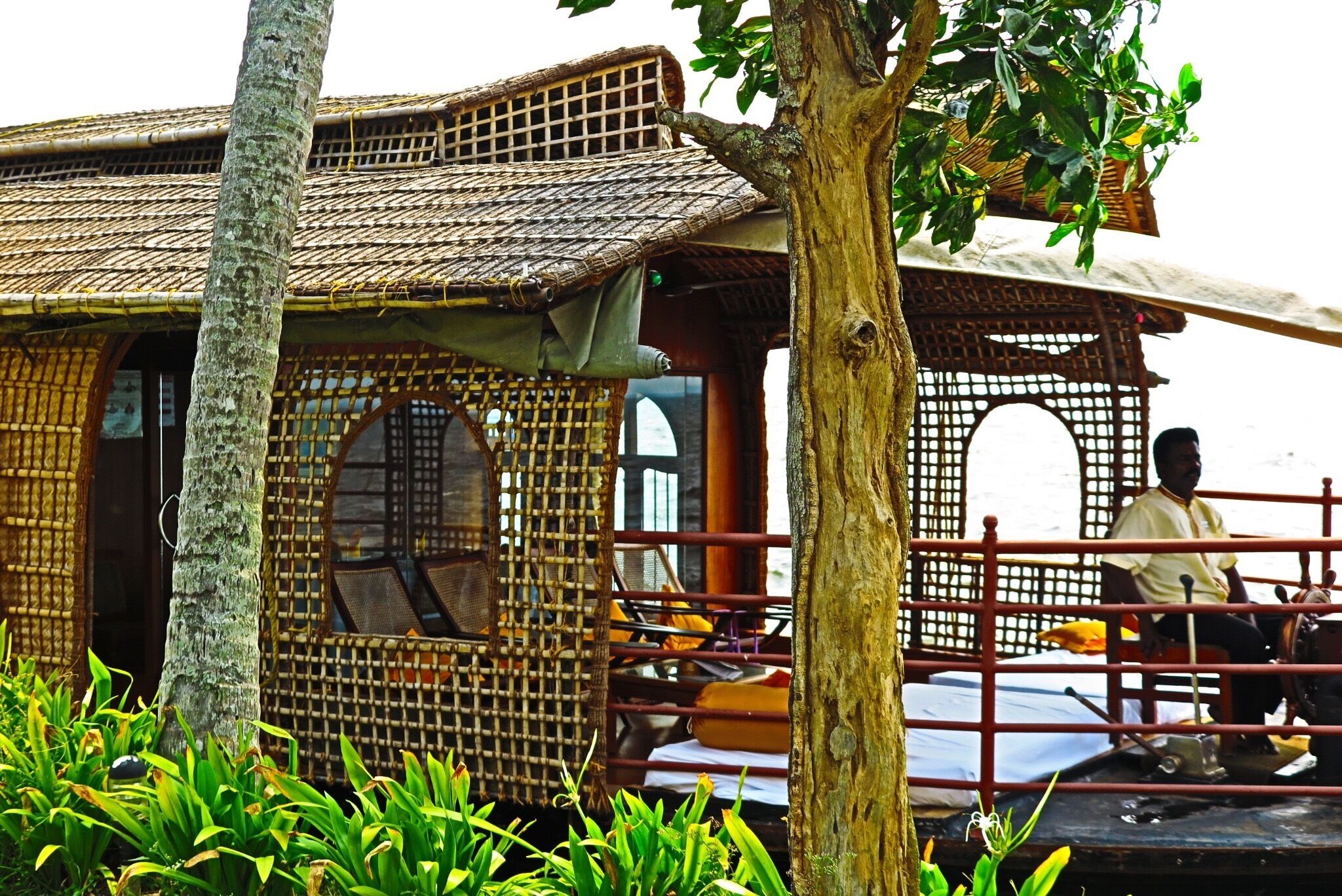 A traditional wooden house with a thatched roof, surrounded by lush greenery.