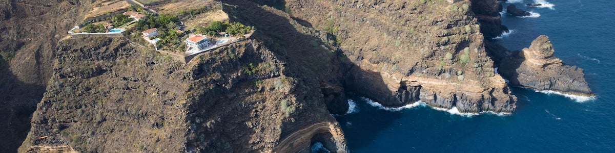 A coastal cliff with a rugged coastline, terraced vineyards, and a small settlement with buildings.