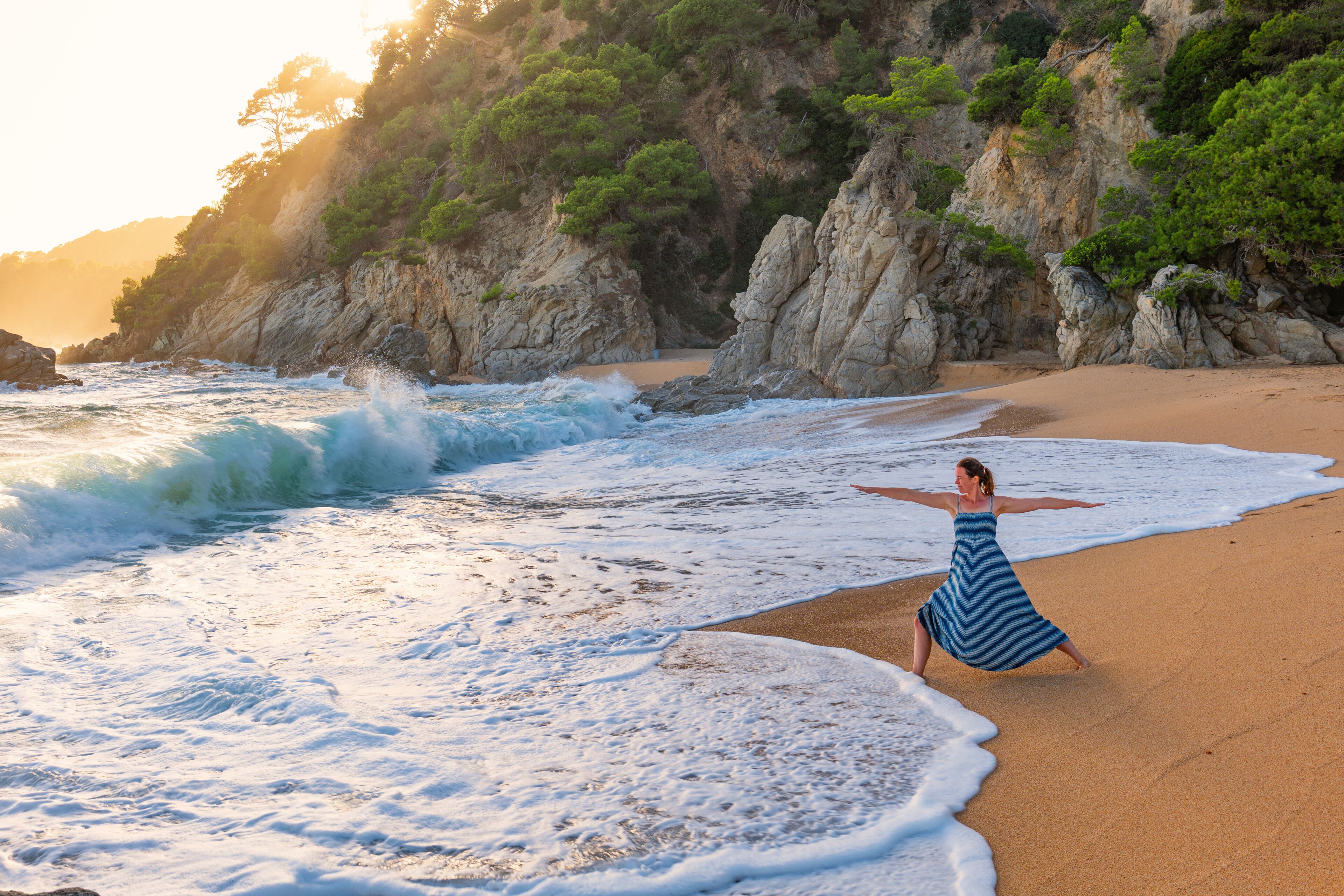 Una playa con olas, una mujer con vestido azul y acantilados rocosos con vegetación.