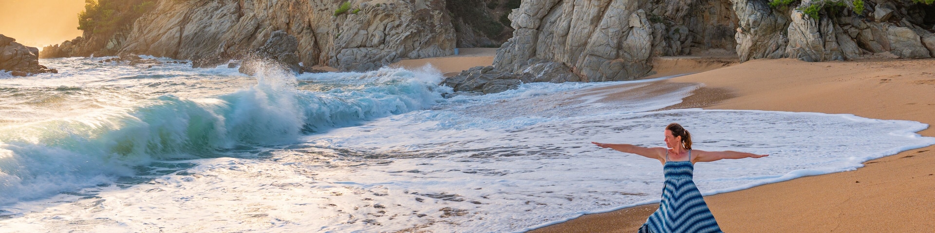 Una playa con olas, una mujer con vestido azul y acantilados rocosos con vegetación.