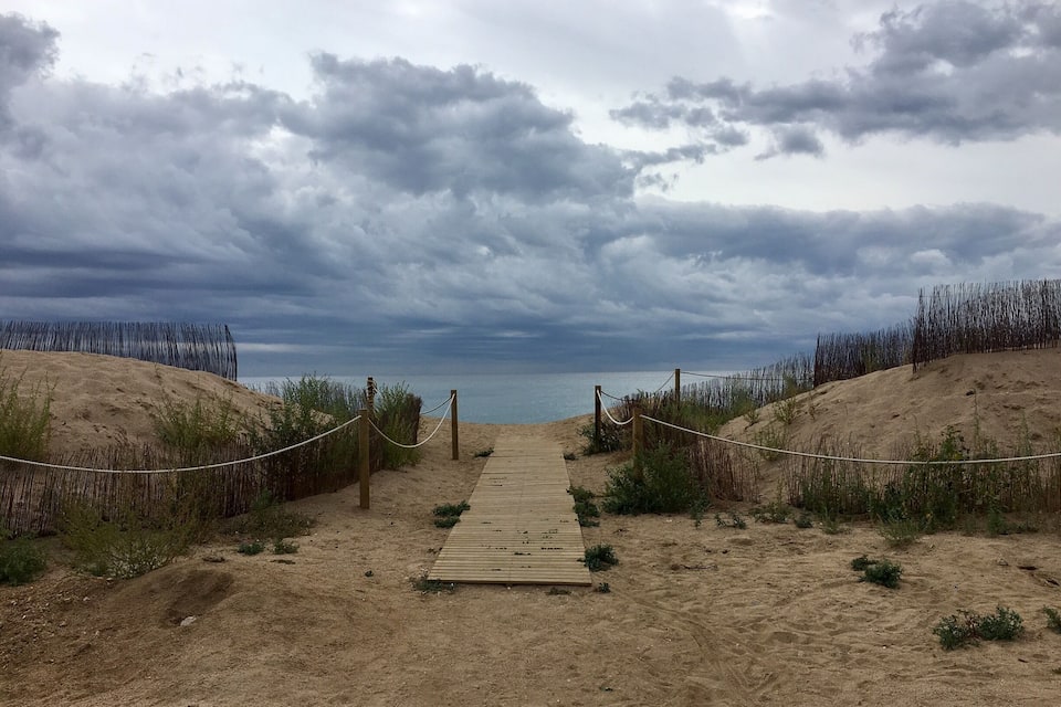 Ein Sandstrand mit einem hölzernen Promenadweg, der zum Wasser führt, umgeben von Dünen und Seilen.