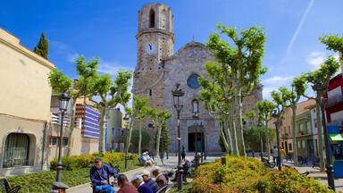 A historic church with a bell tower, surrounded by trees and benches in a sunny plaza.