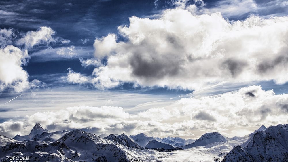 Une chaîne de montagnes enneigée sous un ciel partiellement nuageux.