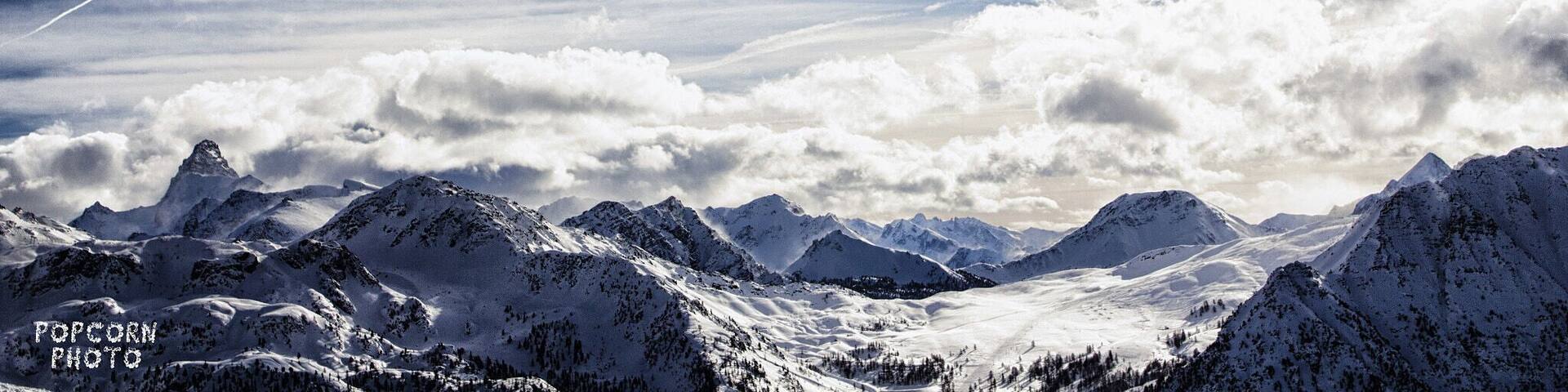 A snow-covered mountain range with a partly cloudy sky.