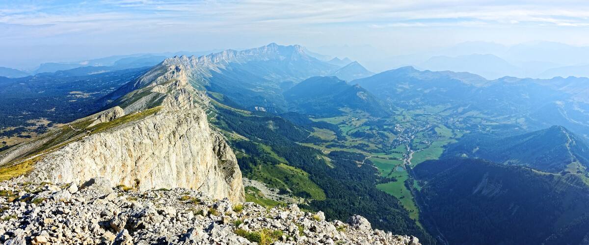 A mountain ridge with a rocky foreground and a valley with green fields and scattered buildings.