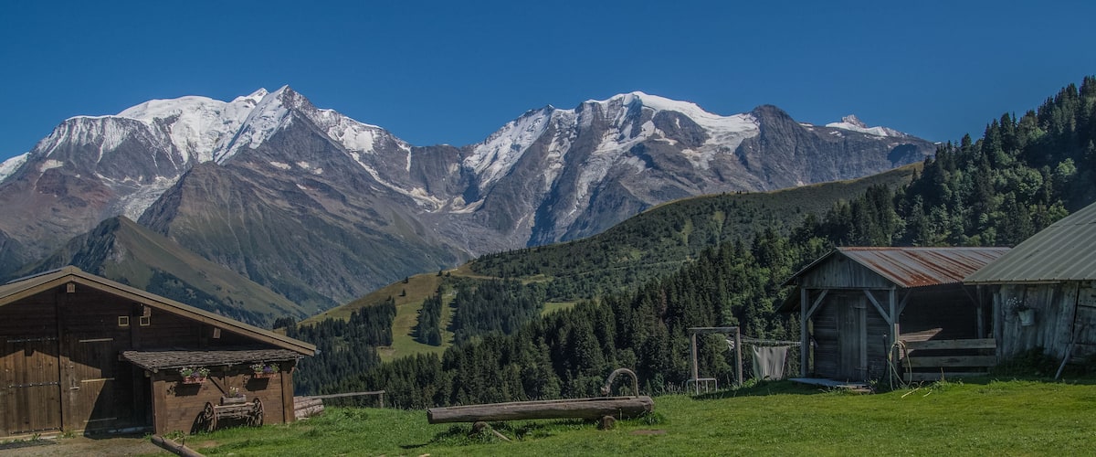 A mountain landscape with snow-capped peaks, a wooden barn, and a green valley.