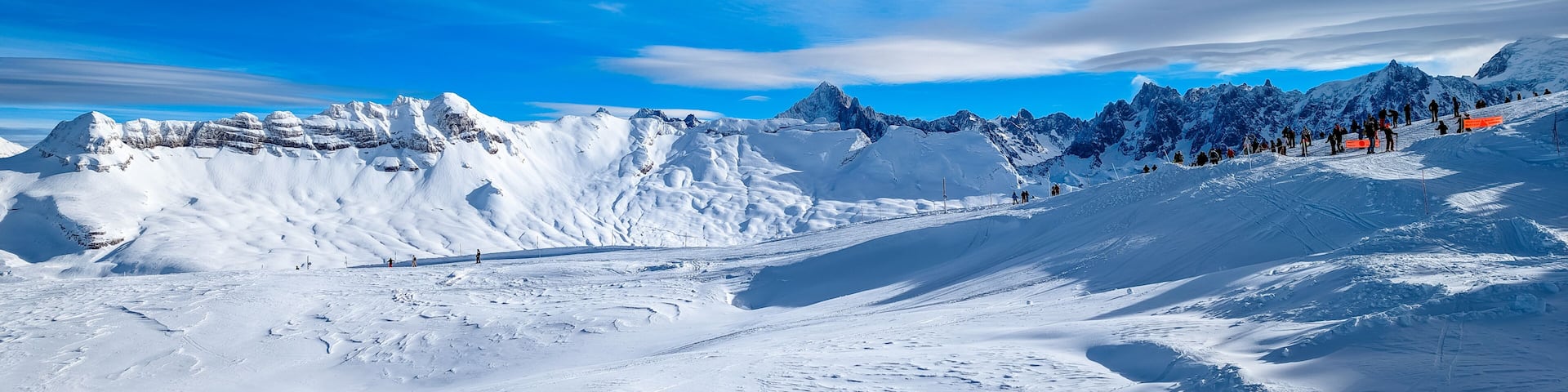 A snow-covered mountain landscape with ski tracks and a clear blue sky.