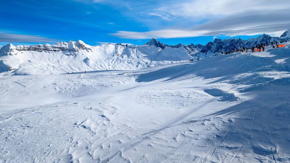 A snow-covered mountain landscape with ski tracks and a clear blue sky.