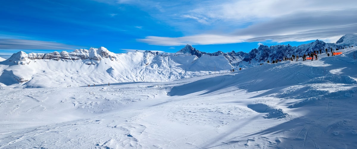 A snow-covered mountain landscape with ski tracks and a clear blue sky.