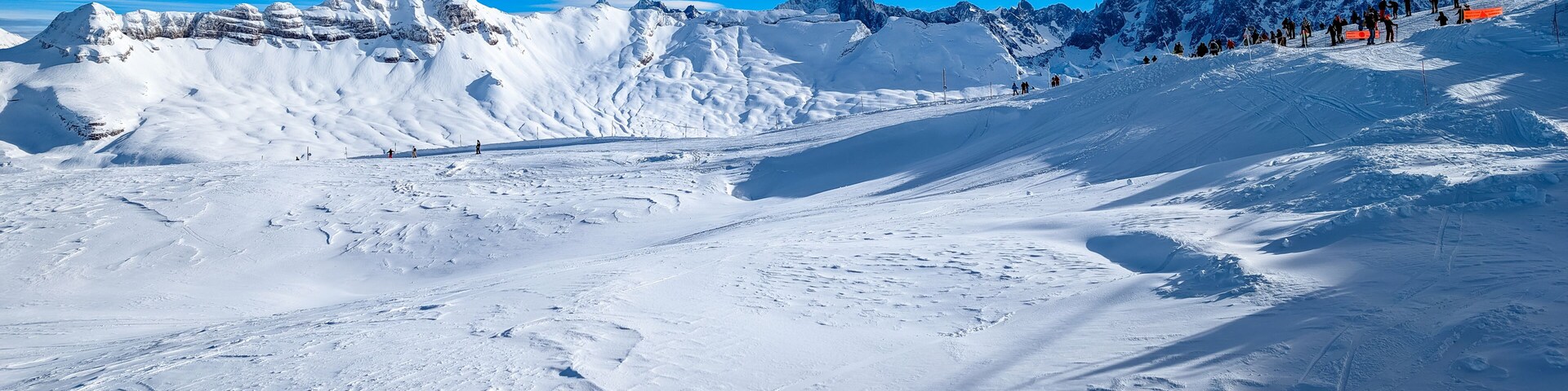 A snow-covered mountain landscape with ski tracks and a clear blue sky.
