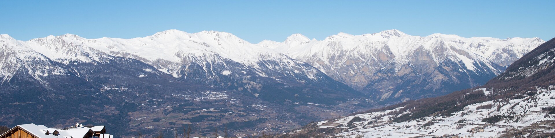 A snow-covered mountain village with wooden buildings and a clear blue sky.