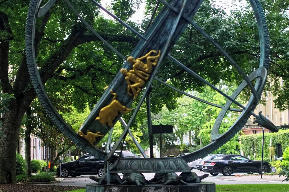 Una gran escultura circular amb figures daurades, situada a un parc amb arbres i un camí de pedra.