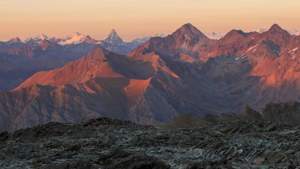 A mountain range with rugged peaks and a rocky foreground.