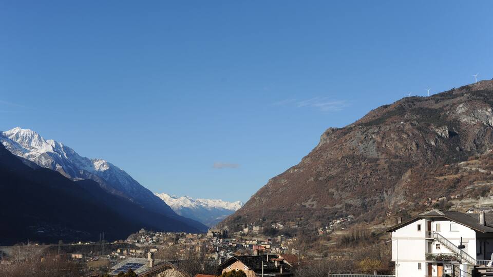 A mountainous landscape with snow-capped peaks, a town nestled in the valley, and wind turbines on the slopes.