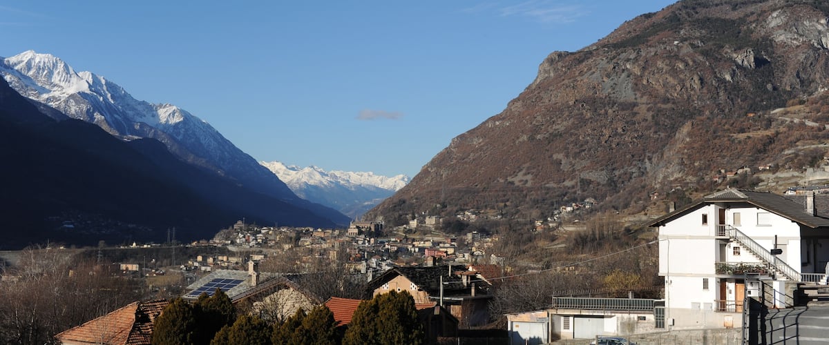 A mountainous landscape with snow-capped peaks, a town nestled in the valley, and wind turbines on the slopes.
