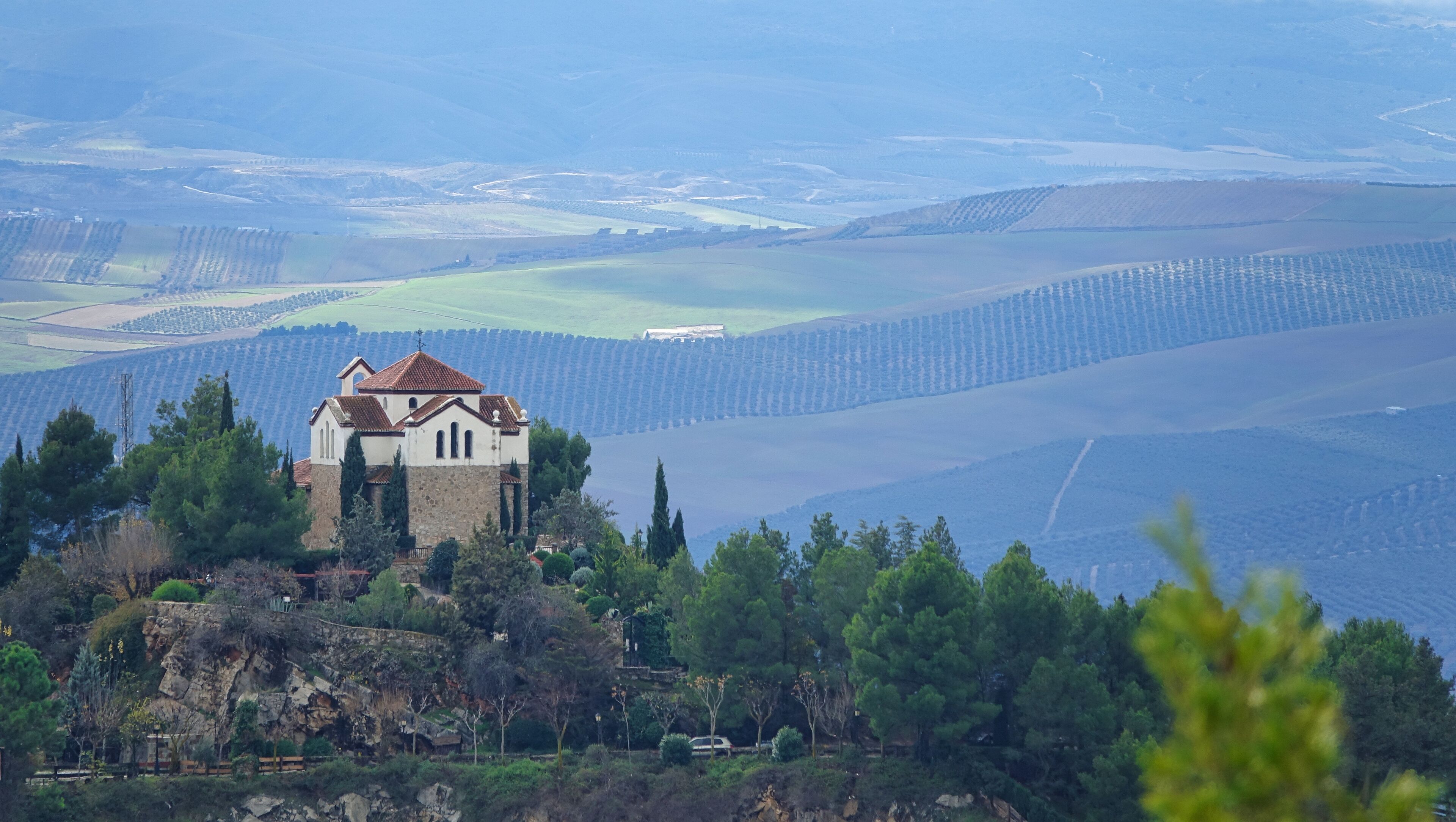 Hermitage of Tres Juanes (Granada) among pine trees on a high rock with the plain in the background on a cloudy day