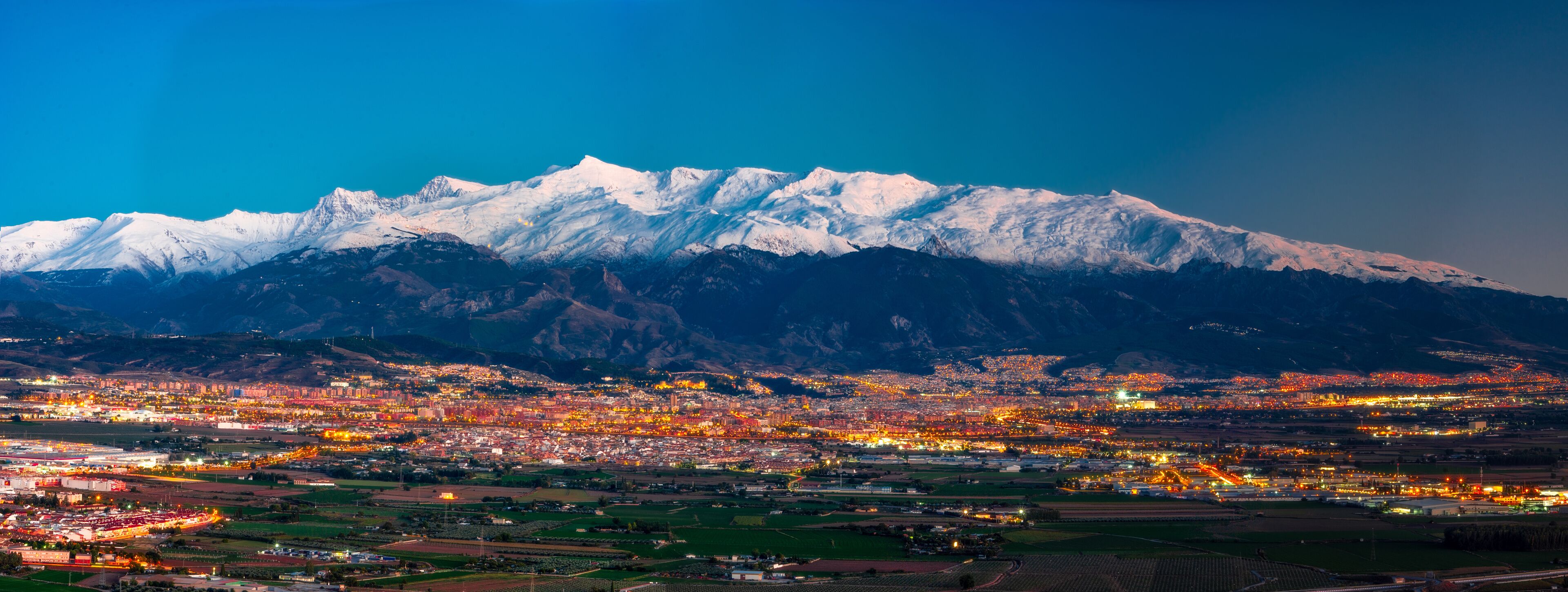 A snow-capped mountain range with a city illuminated in the foreground.