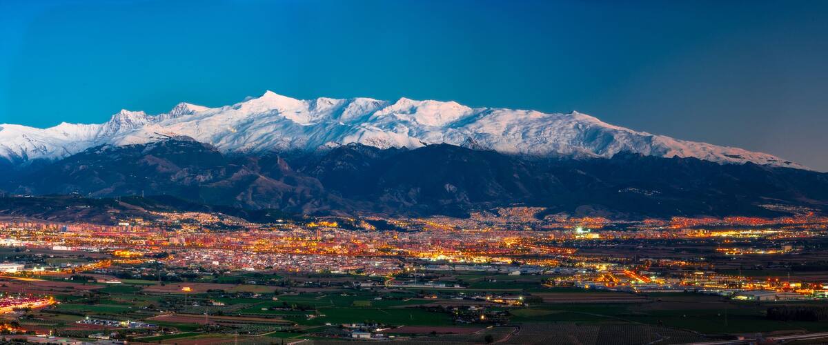 A snow-capped mountain range with a city illuminated in the foreground.
