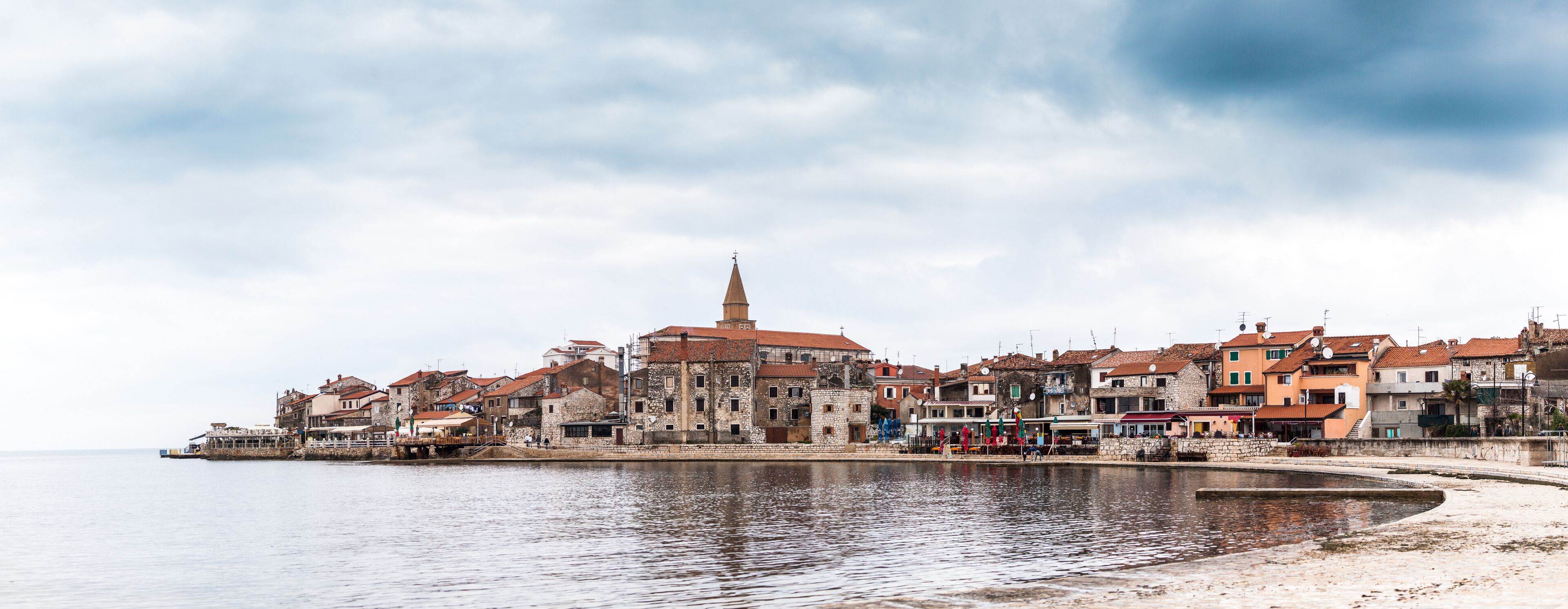 A coastal town with historic buildings, a prominent church tower, and a calm waterfront.
