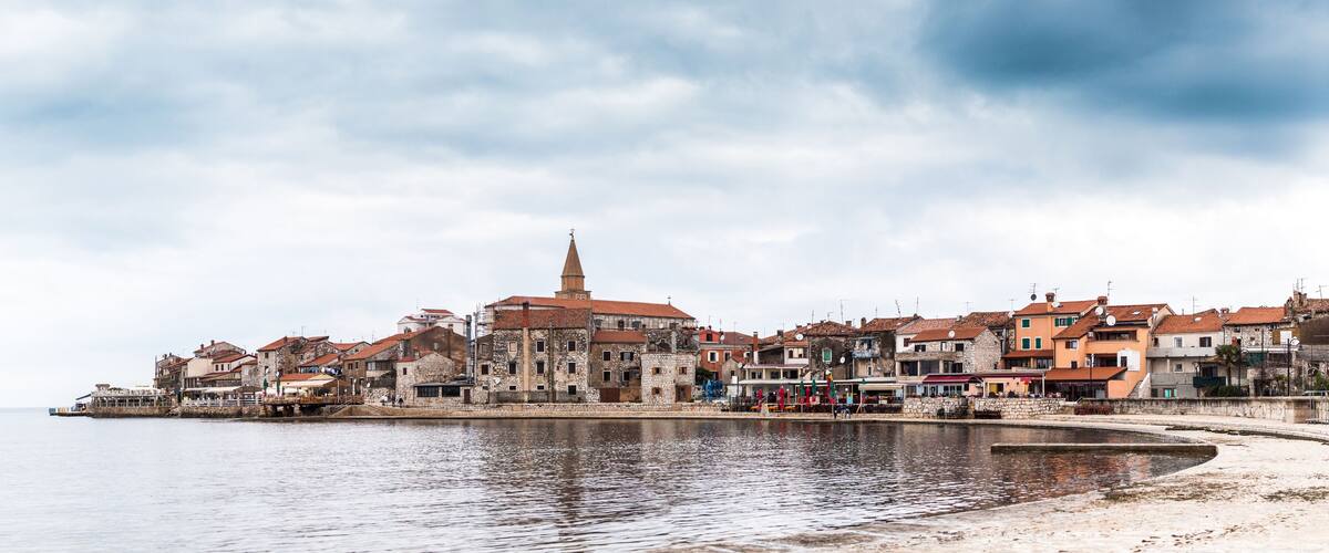 A coastal town with historic buildings, a prominent church tower, and a calm waterfront.