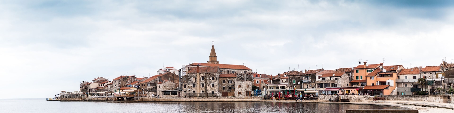 A coastal town with historic buildings, a prominent church tower, and a calm waterfront.