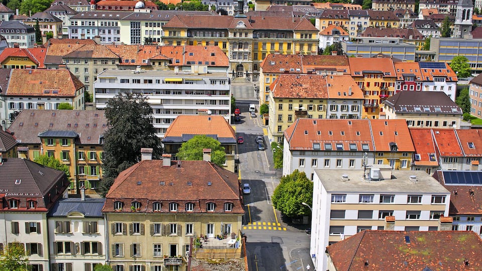 A densely packed urban area with historic buildings, red-tiled roofs, and a central street.