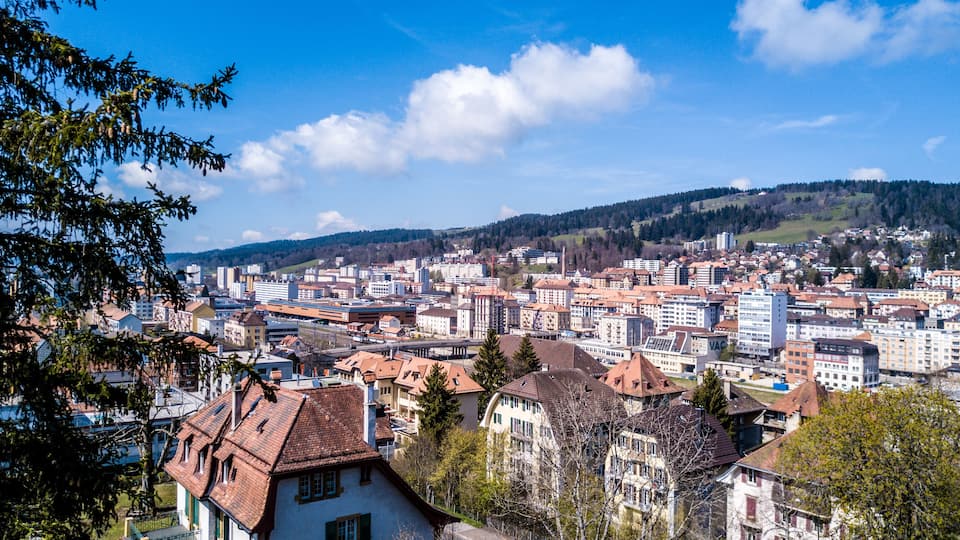 A cityscape with a mix of modern and traditional architecture, surrounded by hills and clear skies.