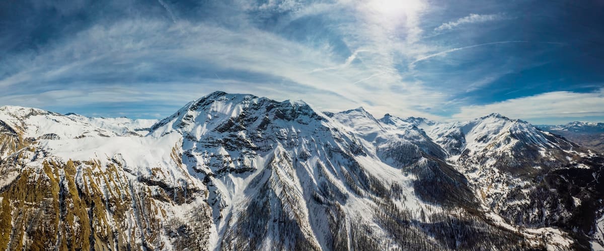 A snow-covered mountain range with a prominent peak, forested valleys, and a clear sky.