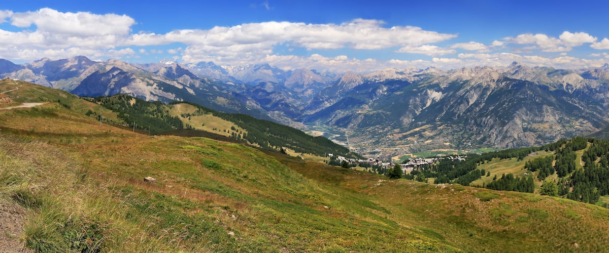 A mountainous landscape with a valley, green hills, and distant snow-capped peaks.