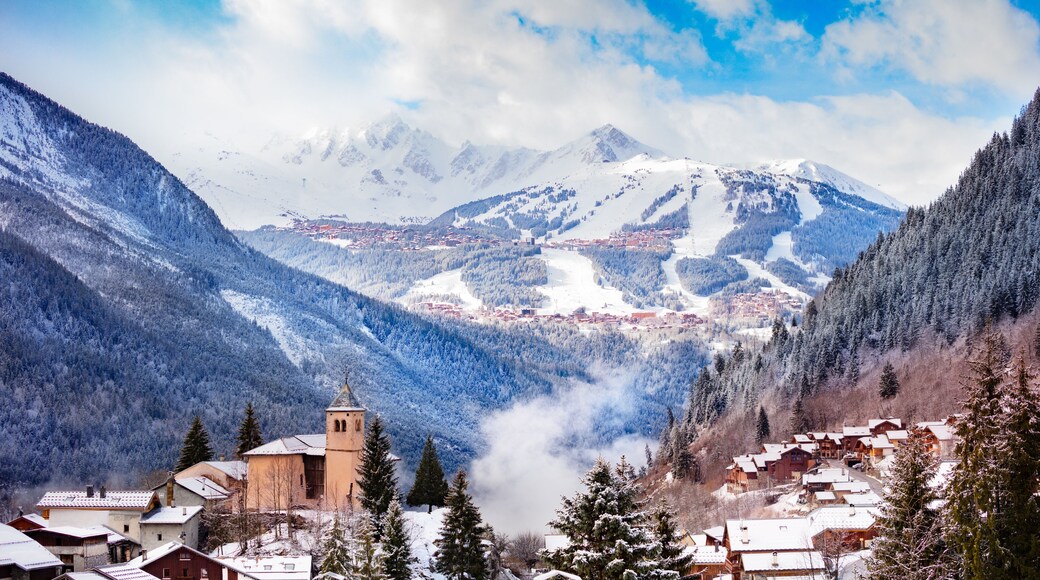 Panorama of Champagny-en-Vanoise village with mist and clouds around old church, over Courchevel resort on background