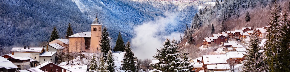 Un village de montagne enneigé, avec une église, des maisons et une piste de ski.