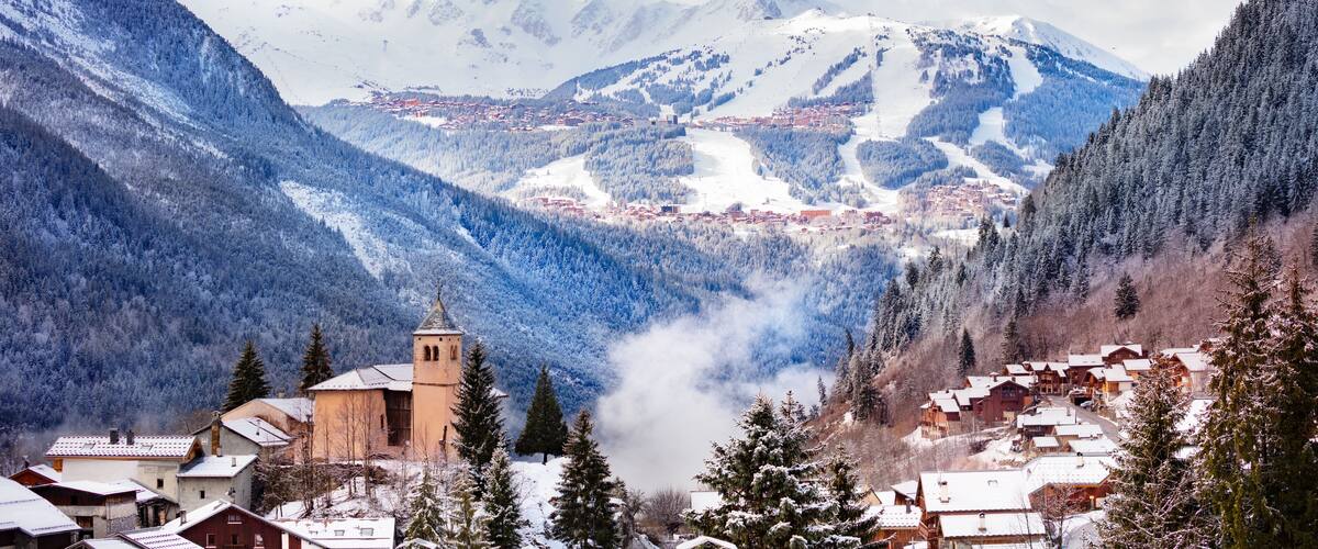 A snow-covered mountain village with a church, houses, and a ski slope.