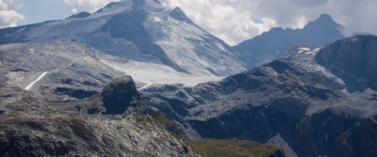 A rugged mountain landscape with a winding road and a glacier.