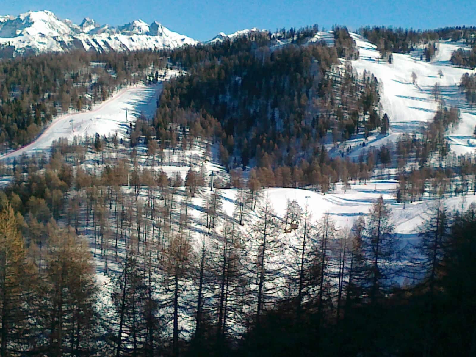 A snow-covered mountain landscape with a ski slope and dense forest.