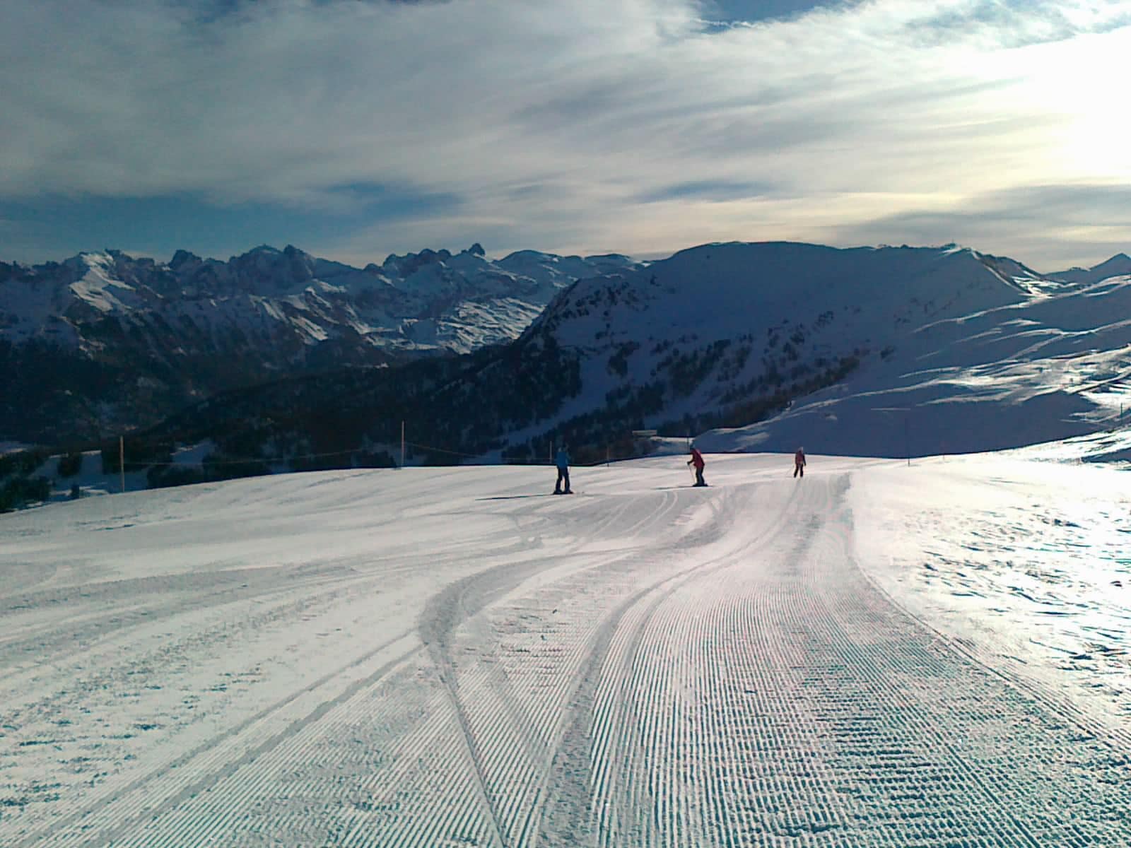 A snowy ski slope with skiers and a mountain range in the background.
