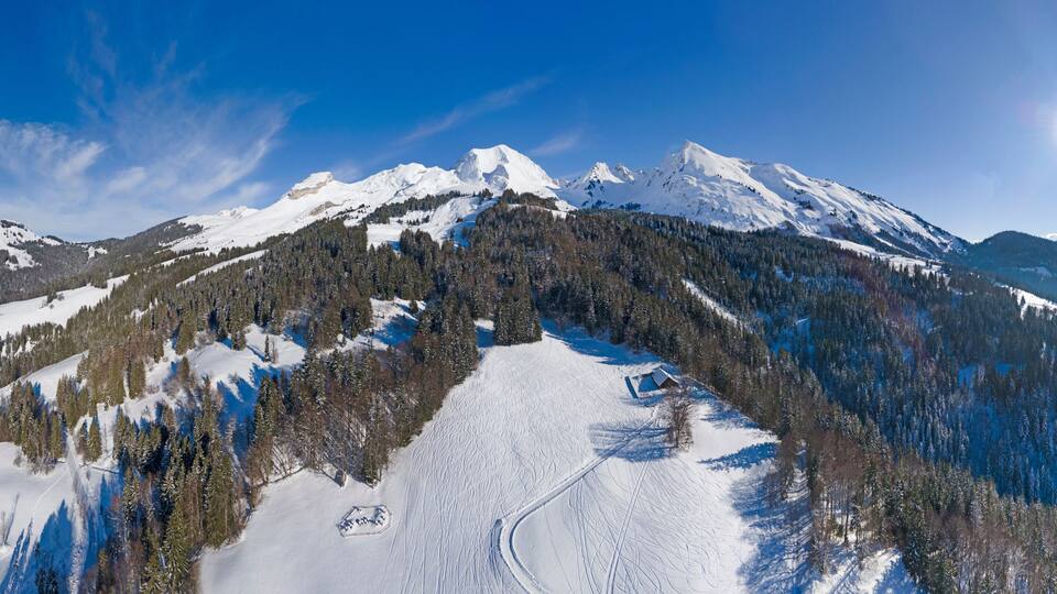 A snow-covered mountain range with a clear sky and a sun shining.