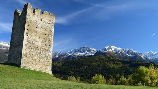 Une tour de pierre se dresse sur une colline verdoyante, avec des montagnes enneigées en arrière-plan.