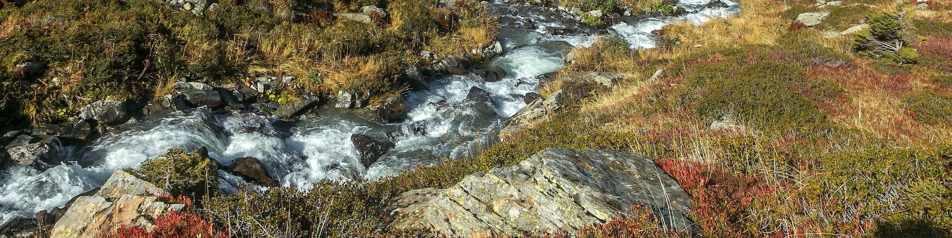 A river flowing through a mountainous landscape with autumn foliage and clouds above.