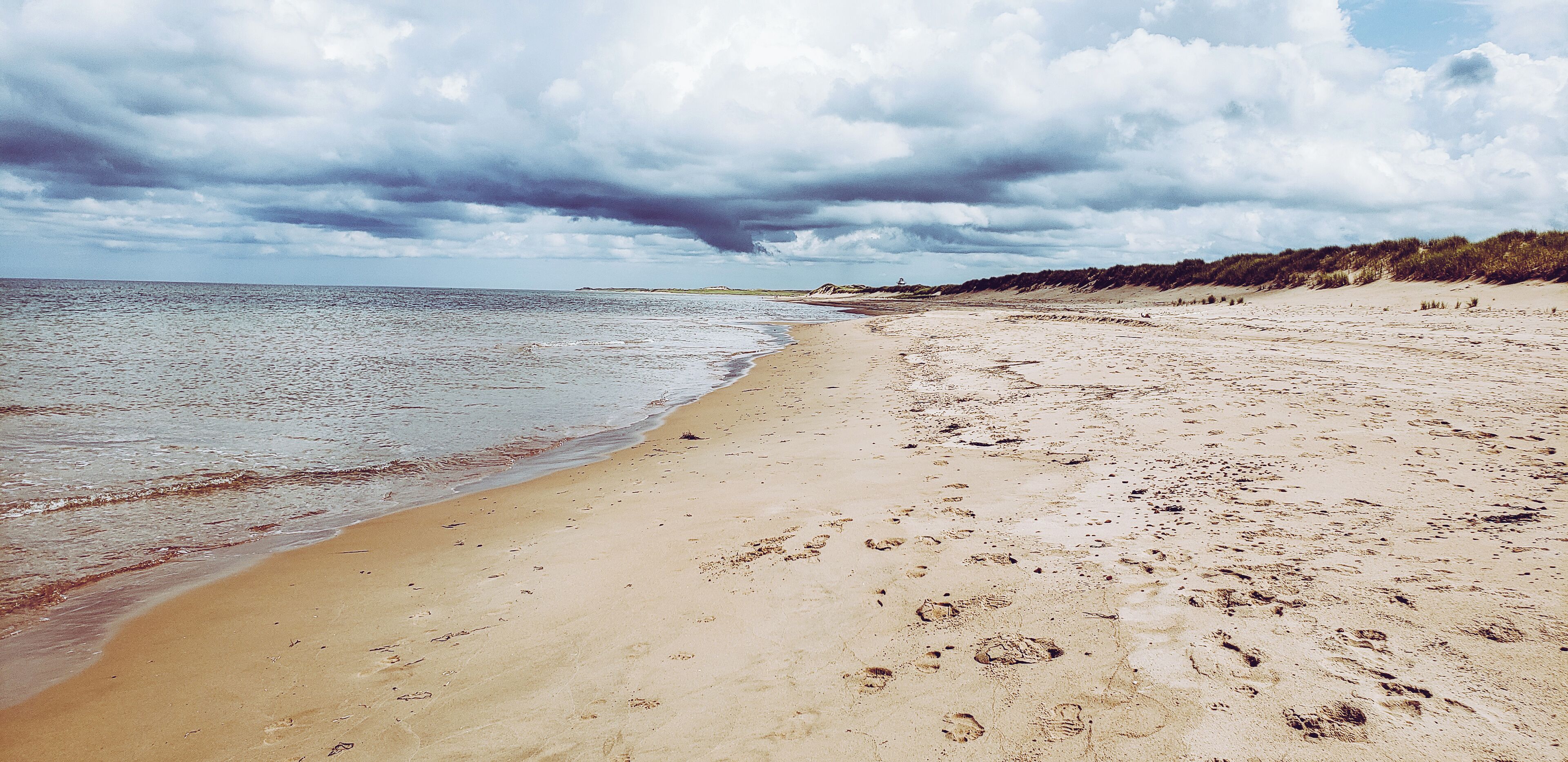 A sandy beach with footprints and a cloudy sky.